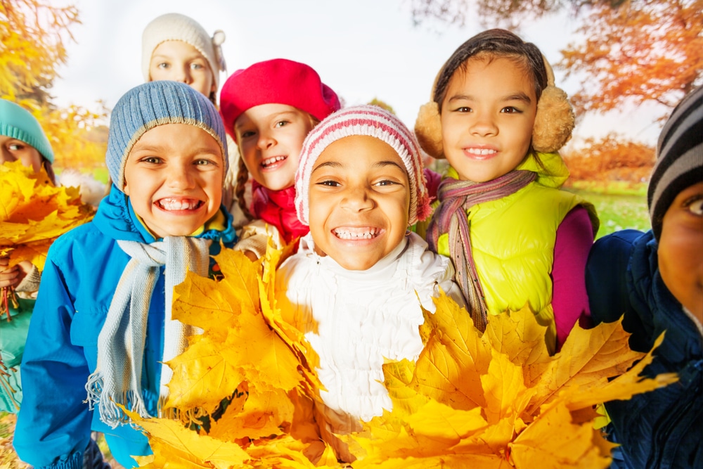 Image of young children with fall leaves for fall writing prompts.